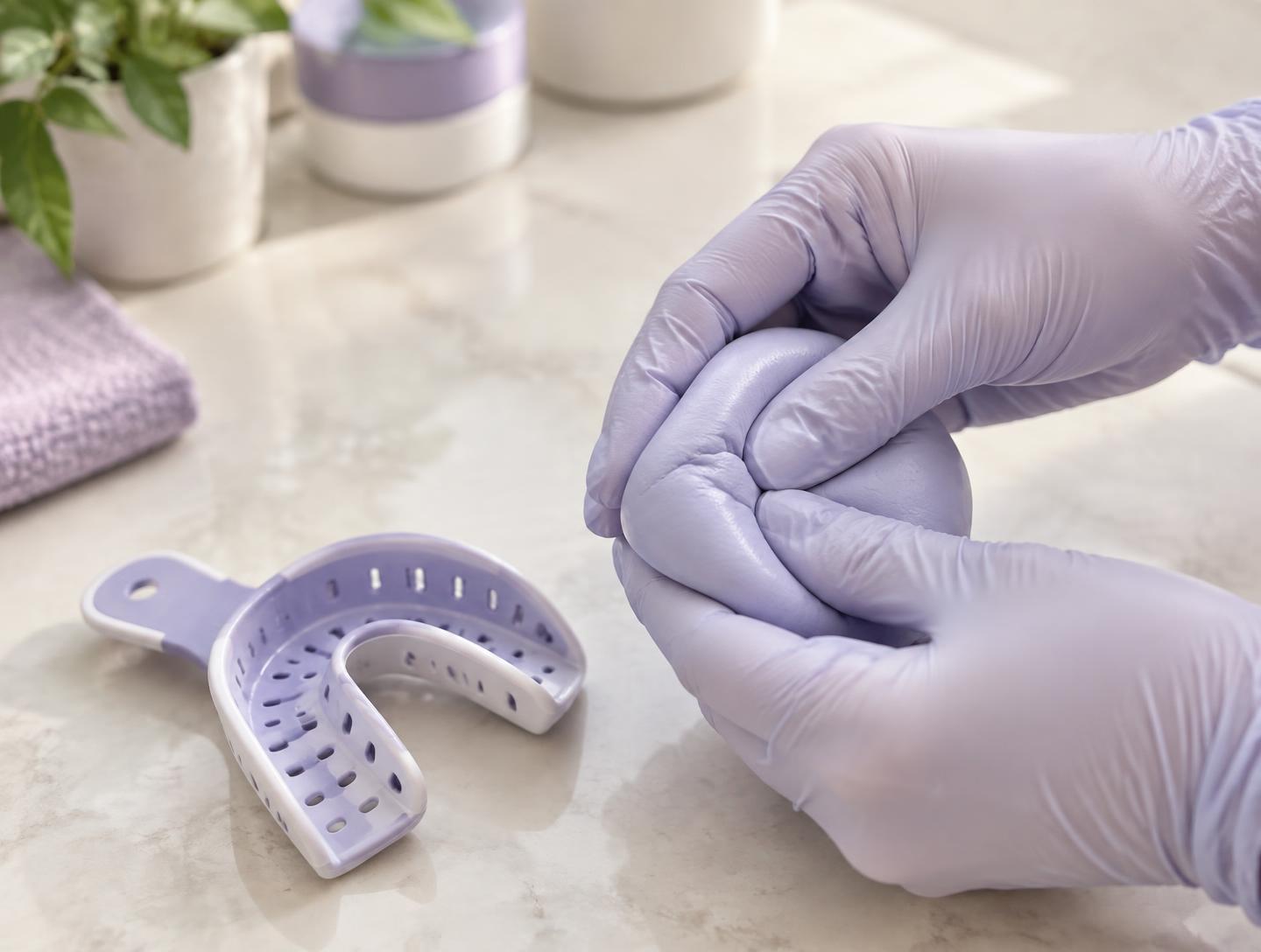 Gloved hands mixing impression putty beside a tray